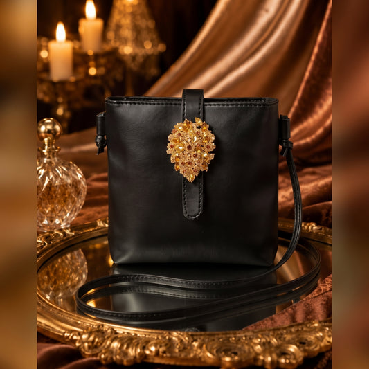 A black faux-leather evening bag with zip and a gold floral brooch closure.