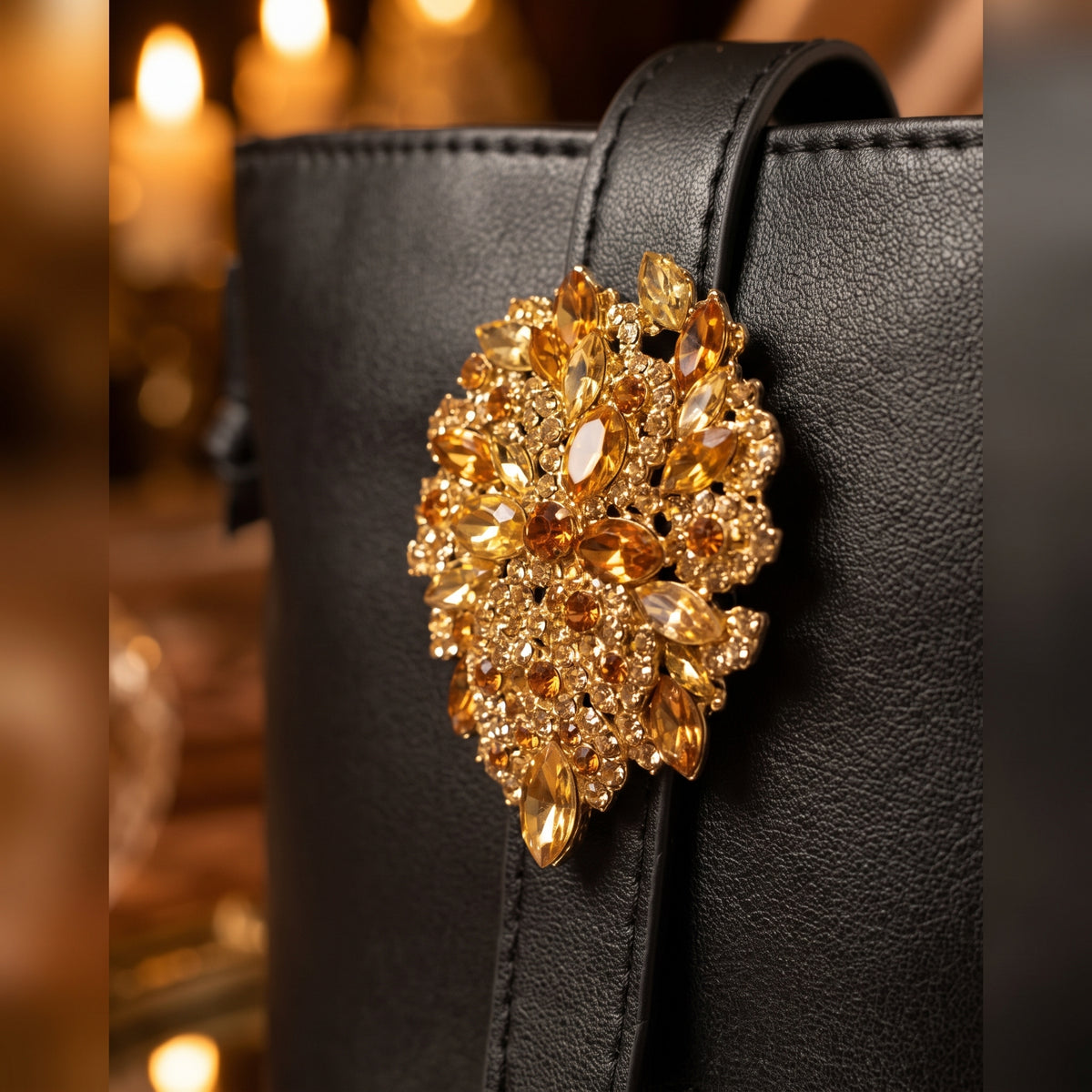 A close-up of a black crossbody evening bag featuring a large, ornate gold-tone brooch embellished with marquise and round amber-colored crystals.