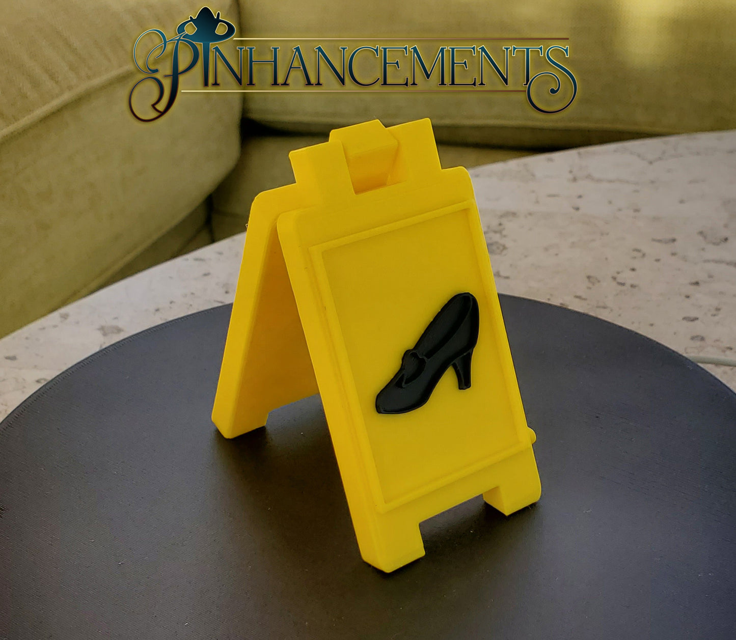 Yellow caution sign with Cinderella slipper, branded 'Pin Enhancements'.