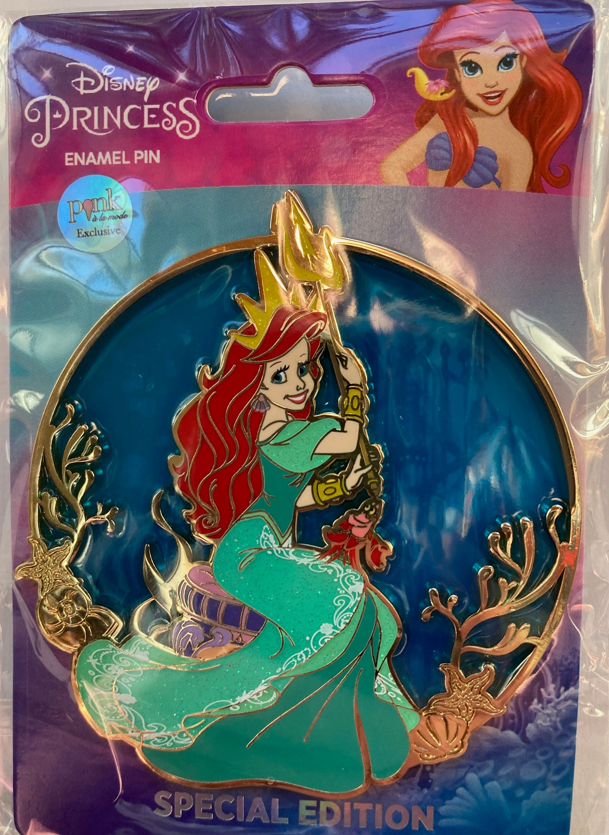 Disney Princess Ariel Special Edition enamel pin in its original retail packaging. The circular pin features Ariel with her signature red hair, green dress, and gold crown holding Triton's trident, set against an underwater scene with gold coral details.