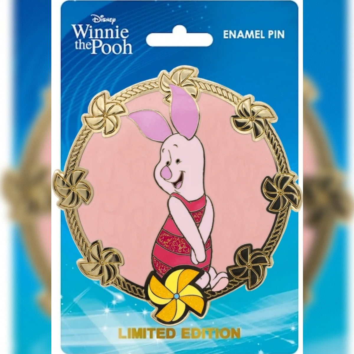 Disney Winnie the Pooh enamel pin in its original blue backing card packaging. The pin features Piglet sitting inside a gold circular frame set against a pink background with a pinwheel at the bottom.