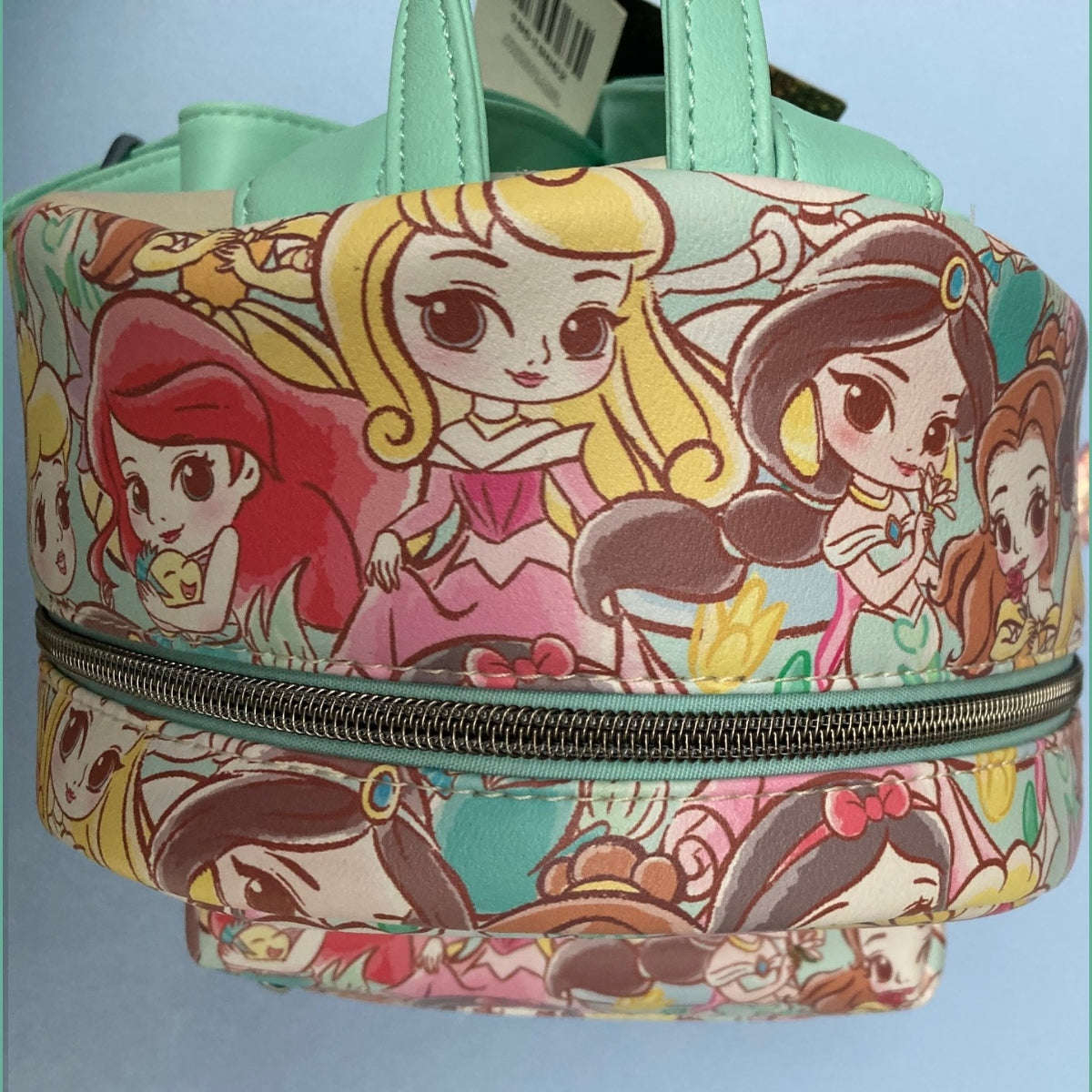 The top crown of a Disney Loungefly mini backpack featuring an all-over colorful Chibi princess print, highlighting quality views of Ariel, Aurora, Jasmine, and Belle with original tags visible.