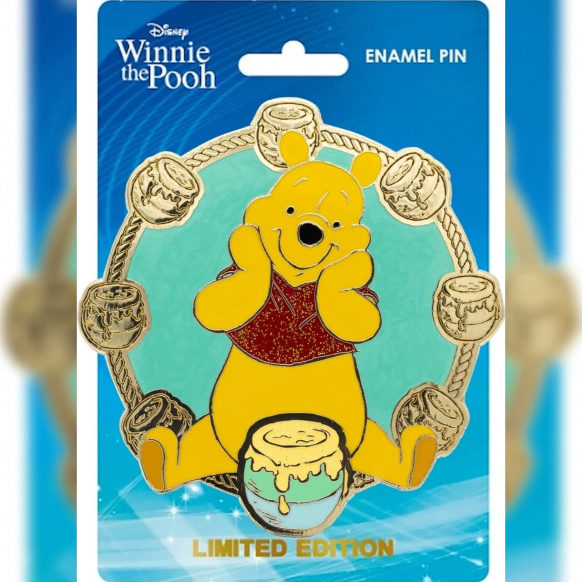 Disney Winnie the Pooh enamel pin on its original blue backing card, featuring a limited edition design of Winnie the Pooh with a honey pot and more honey pots around him.