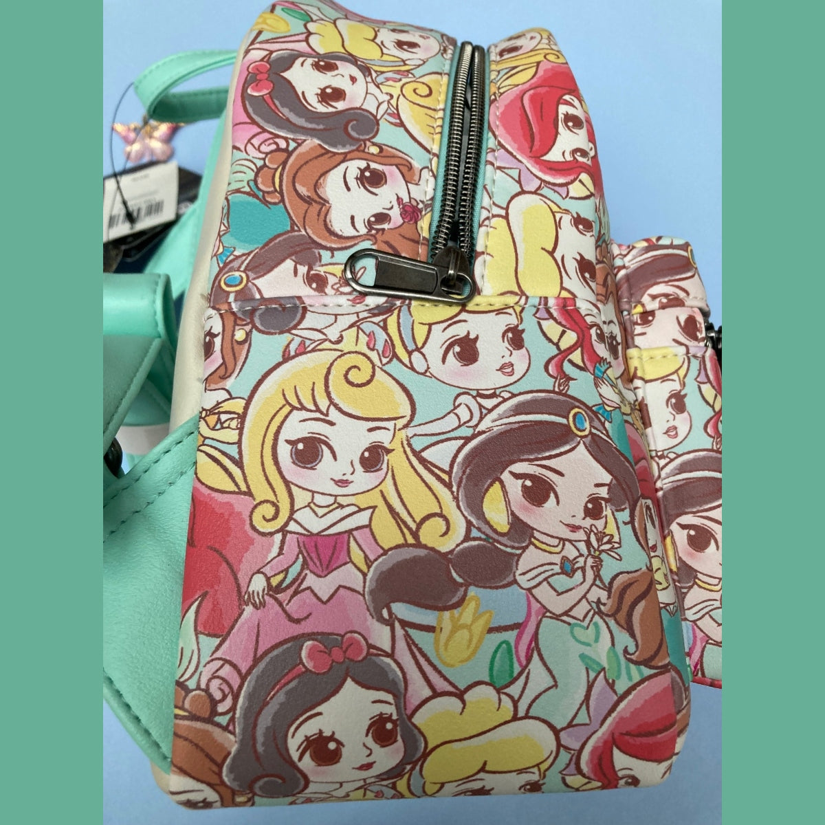 A Disney Loungefly mini backpack opposite side view featuring an all-over colorful Chibi princess print with teal faux-leather straps and trim, shown against a light blue background with teal side borders.